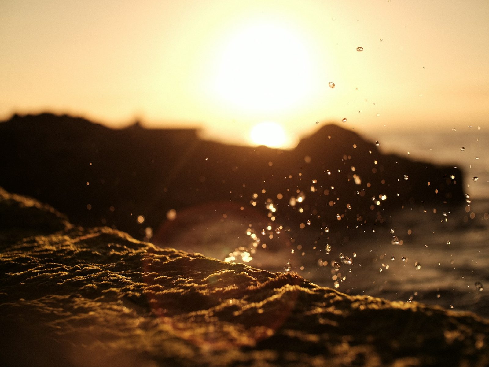 Sunset, sea water hitting the rocks and throwing up glowing drops