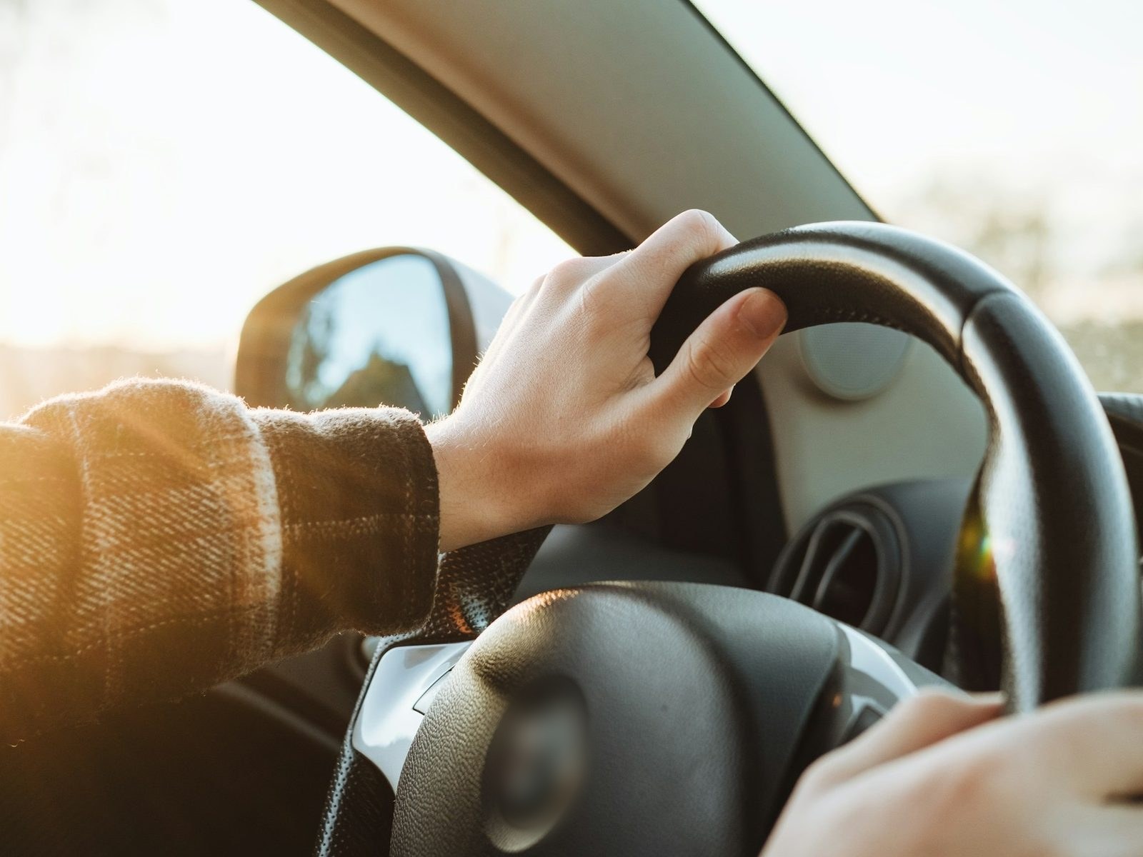 Two hands holding a steering wheel steadily, soft light outside the window