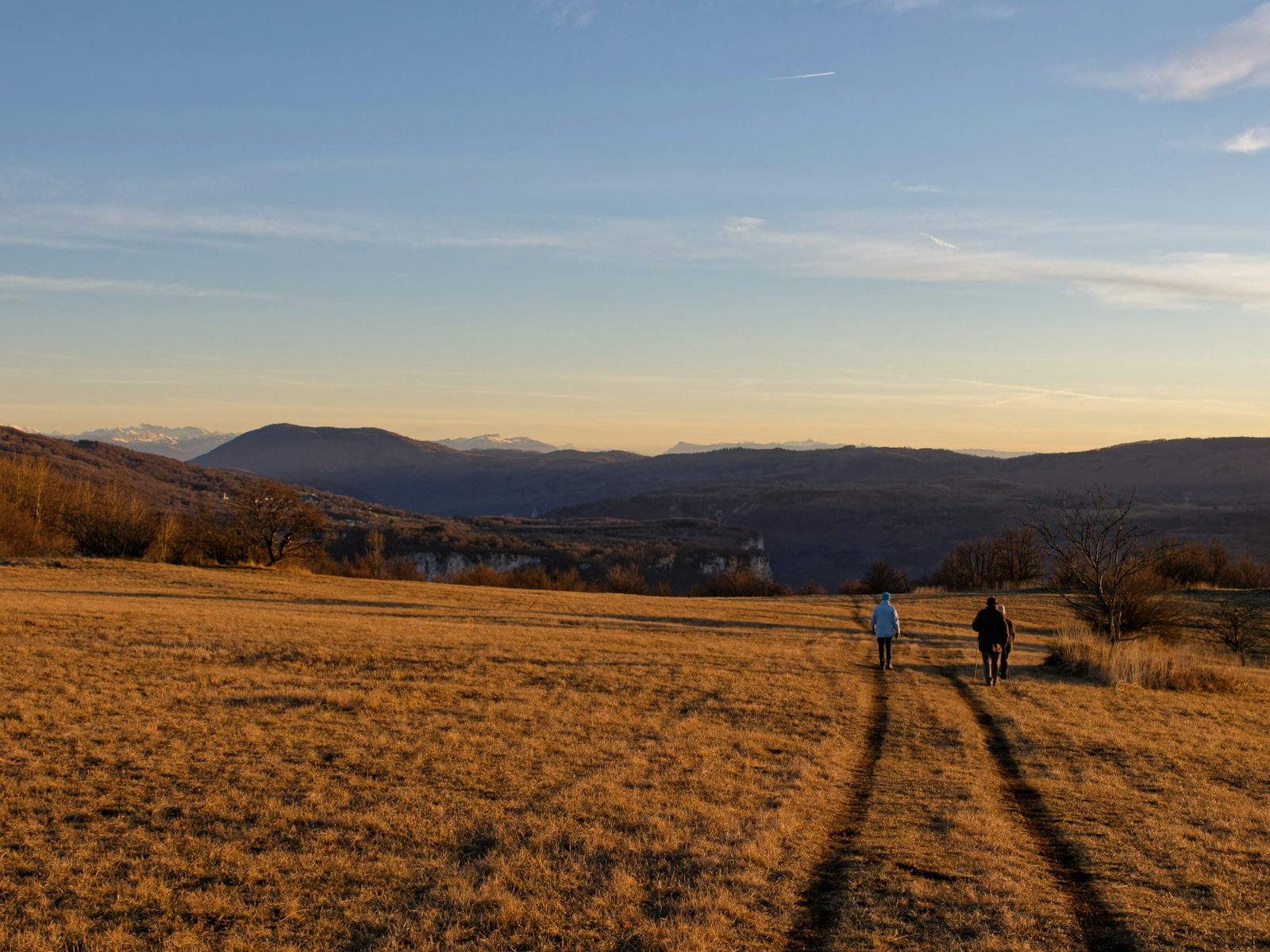 On open grassland, two people each walk along a wheel track into the distance