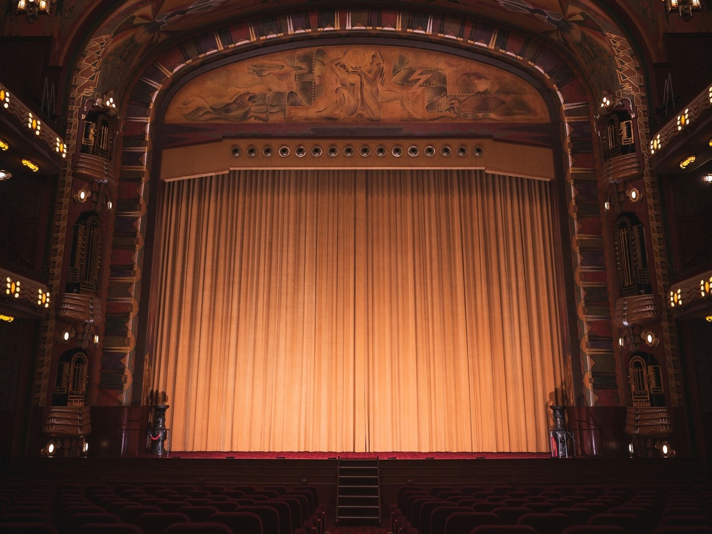 An empty old theatre, the curtain in front of the stage lit by warm golden light